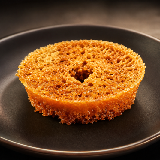 A golden-brown, porous sponge cake slice, resembling a donut, presented on a dark matte ceramic plate.
