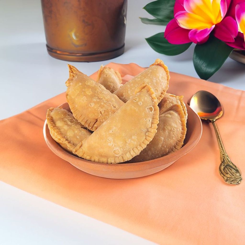 The image depicts "Kajjikayalu," a traditional Indian sweet pastry from Andhra Pradesh, featuring a crispy, golden-brown exterior and a sweet coconut filling. These crescent-shaped treats are deep-fried and often enjoyed during festive occasions.