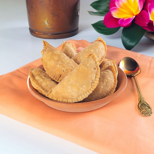 The image depicts "Kajjikayalu," a traditional Indian sweet pastry from Andhra Pradesh, featuring a crispy, golden-brown exterior and a sweet coconut filling. These crescent-shaped treats are deep-fried and often enjoyed during festive occasions.