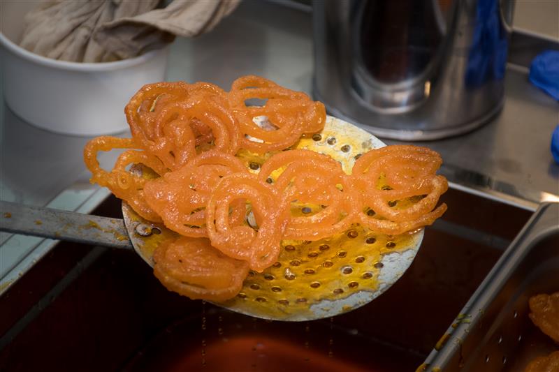 close-up of crispy and sweet fried jalebis being scooped out of hot oil