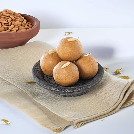 A plate of traditional Andhra Pradesh sweet, Sunnundalu, made from roasted urad dal, jaggery, and nuts, garnished with slivered almonds and pistachios.