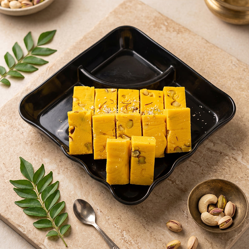 Yellow dessert blocks on a black tray with green leaves and a spoon on a beige surface