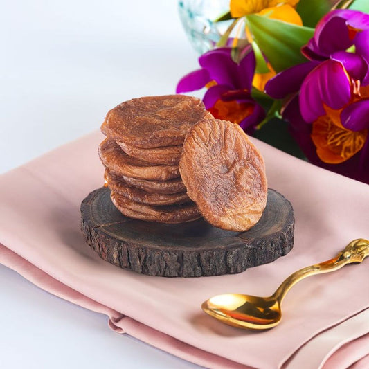 A stack of traditional South Indian Ariselu sweets made with rice, jaggery, and ghee, placed on a wooden slab with a golden spoon and fresh flowers in the background.