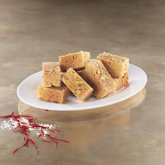 A plate of golden-brown Mysore Pak (Hard) garnished with chopped pistachios, served on a white dish, with saffron strands elegantly placed beside it.